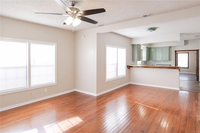 unfurnished living room featuring wood-type flooring, visible vents, baseboards, and a healthy amount of sunlight