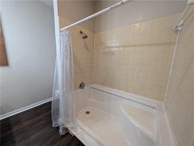 bathroom with baseboards, a textured wall, a shower with shower curtain, and wood finished floors