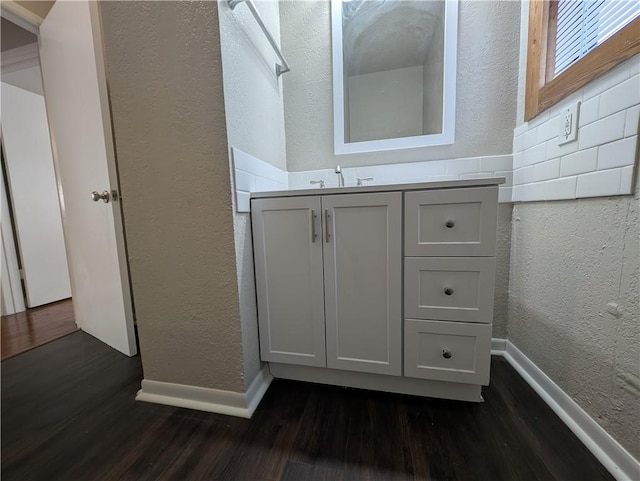 bathroom featuring a textured wall, vanity, baseboards, and wood finished floors