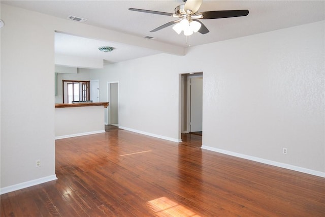 empty room featuring wood-type flooring, visible vents, baseboards, and beamed ceiling