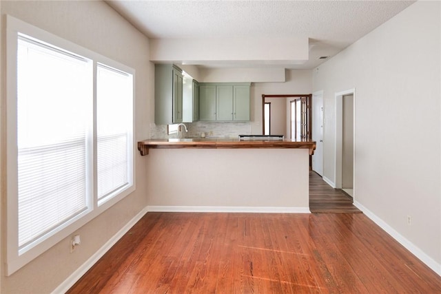 kitchen with green cabinets, a peninsula, tasteful backsplash, and wood finished floors