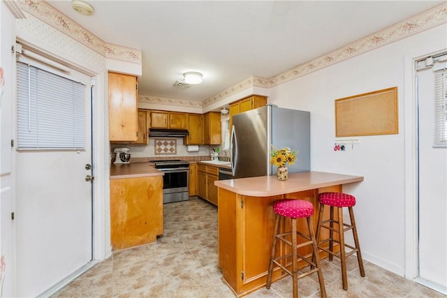 kitchen with visible vents, under cabinet range hood, appliances with stainless steel finishes, a peninsula, and light countertops