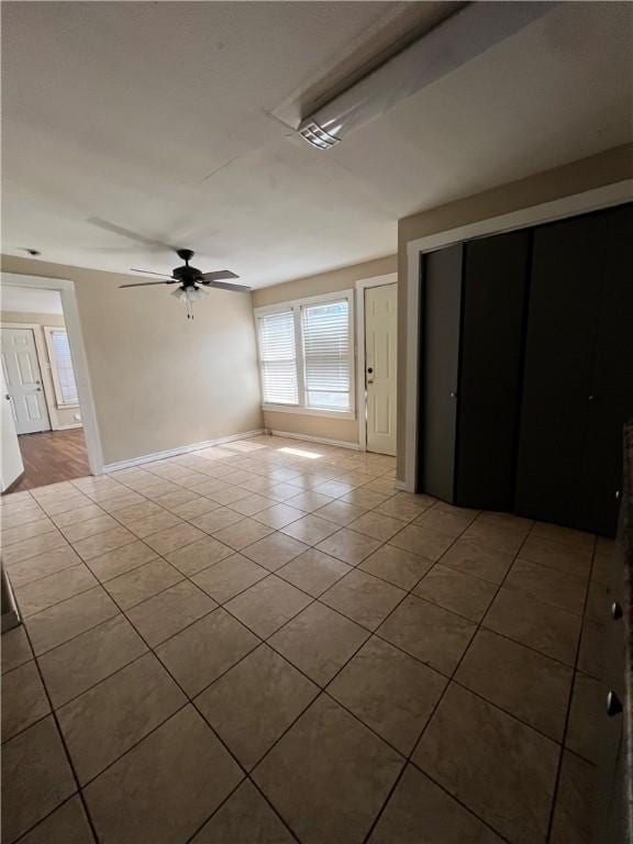 empty room with tile patterned flooring, a ceiling fan, and baseboards