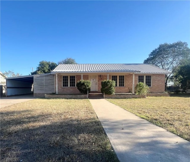 ranch-style home with brick siding, a front yard, metal roof, an attached carport, and driveway