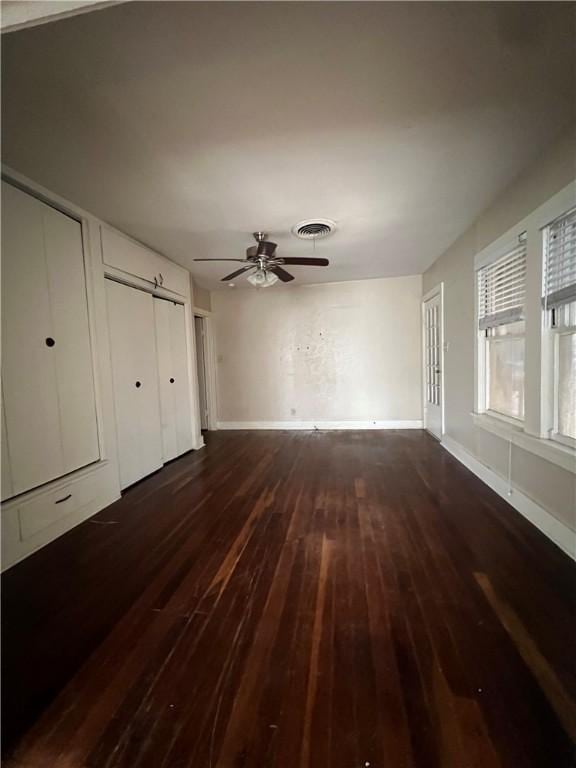 unfurnished bedroom with ceiling fan, dark wood-type flooring, visible vents, baseboards, and two closets