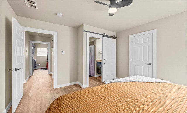 bedroom with a barn door, light wood-style flooring, visible vents, baseboards, and ensuite bath