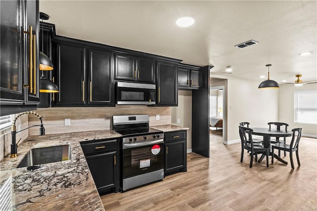 kitchen featuring a sink, appliances with stainless steel finishes, dark cabinetry, backsplash, and light stone countertops