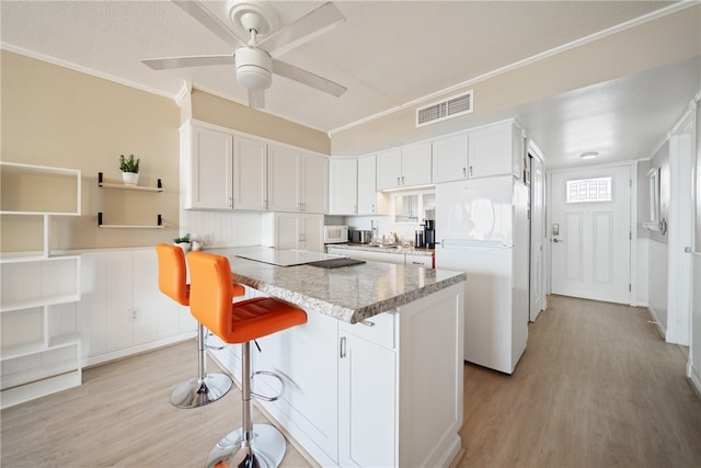 kitchen featuring light wood-type flooring, white appliances, ceiling fan, white cabinets, and a breakfast bar area