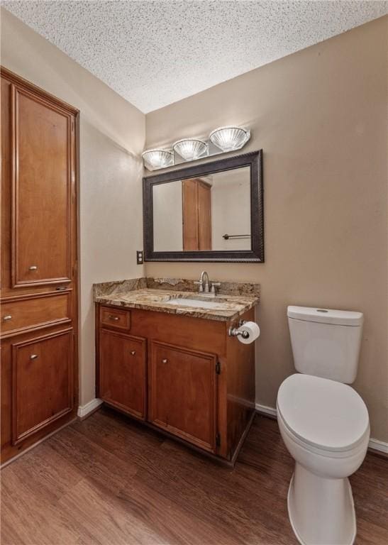 half bathroom featuring vanity, wood finished floors, baseboards, a textured ceiling, and toilet