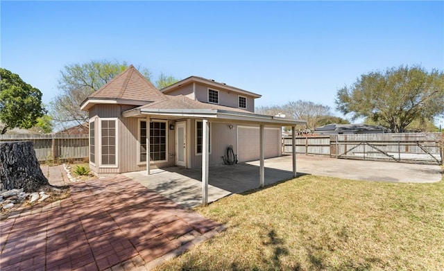 rear view of house with a lawn, a gate, fence, concrete driveway, and a shingled roof