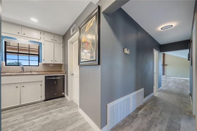 kitchen with white cabinetry, sink, black dishwasher, light hardwood / wood-style flooring, and decorative backsplash