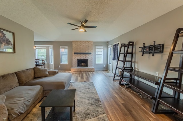 living room featuring a textured ceiling, hardwood / wood-style flooring, a brick fireplace, and ceiling fan