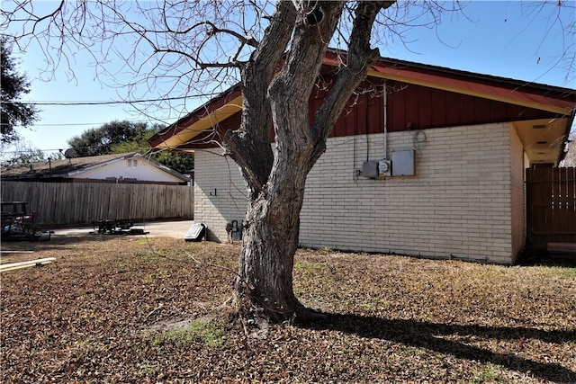 view of side of home featuring board and batten siding, brick siding, and fence