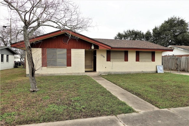 single story home with a front lawn, a shingled roof, fence, and brick siding