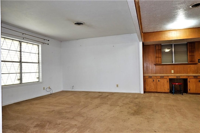 unfurnished room with baseboards, built in desk, visible vents, and light colored carpet