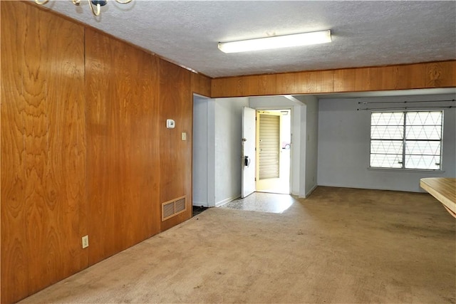 carpeted spare room featuring a textured ceiling, visible vents, and wooden walls