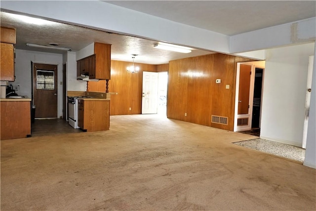 kitchen with pendant lighting, brown cabinets, visible vents, wood walls, and gas range