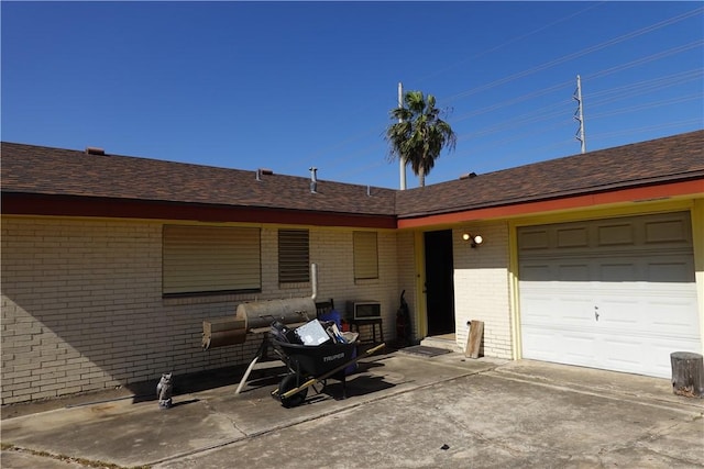 exterior space with an attached garage, a shingled roof, concrete driveway, and brick siding