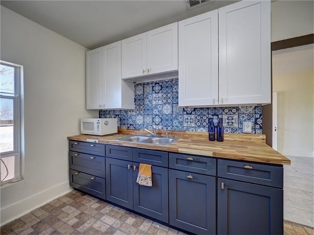 kitchen with backsplash, wooden counters, blue cabinets, sink, and white cabinetry