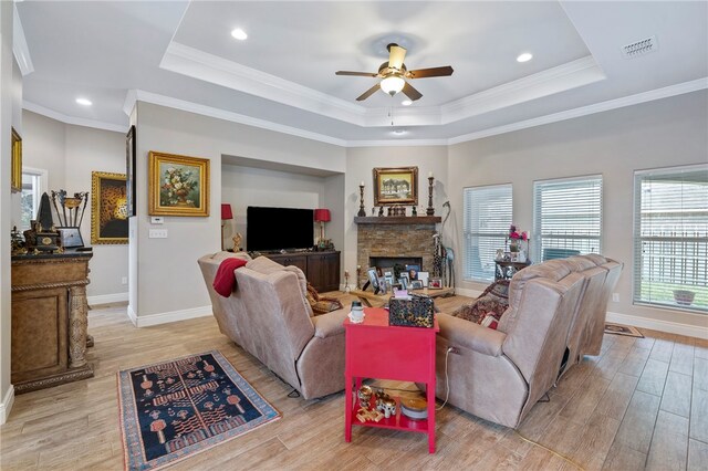 living room with a fireplace, crown molding, a tray ceiling, ceiling fan, and light hardwood / wood-style flooring