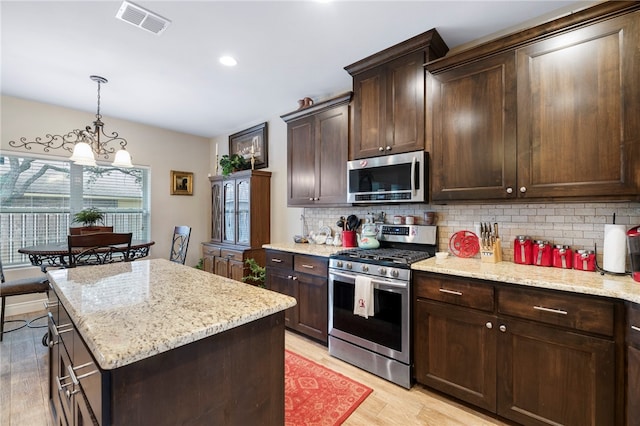 kitchen featuring a center island, stainless steel appliances, dark brown cabinetry, an inviting chandelier, and light hardwood / wood-style flooring