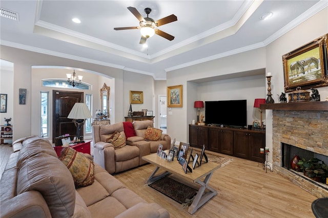 living room featuring light hardwood / wood-style floors, ceiling fan with notable chandelier, a fireplace, a raised ceiling, and crown molding