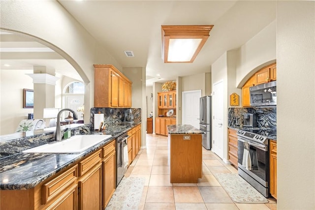 kitchen with visible vents, dark stone counters, a center island, stainless steel appliances, and a sink