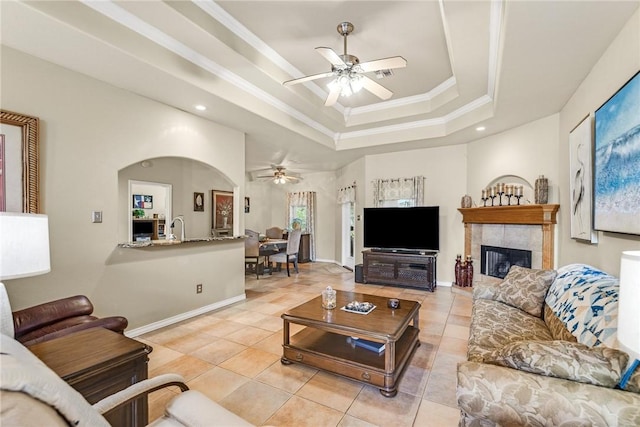 living room featuring a tray ceiling, ornamental molding, light tile patterned flooring, ceiling fan, and baseboards