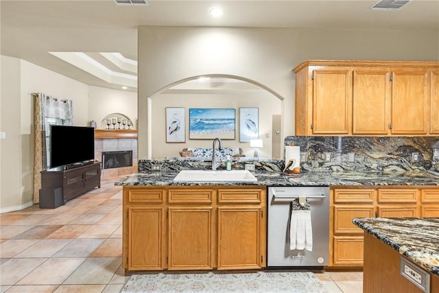 kitchen featuring decorative backsplash, light tile patterned flooring, a sink, dark stone countertops, and dishwasher