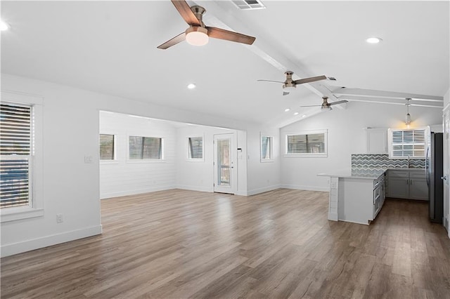 unfurnished living room featuring vaulted ceiling with beams, light wood finished floors, plenty of natural light, and baseboards