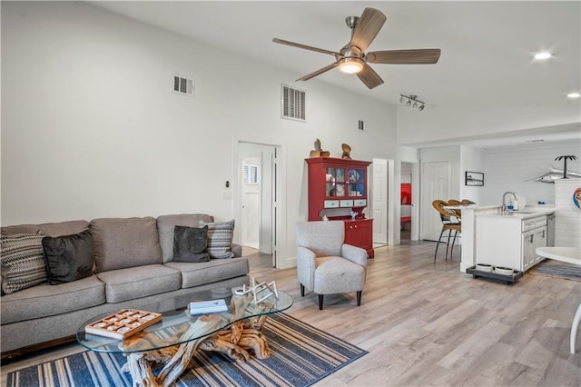 living area featuring lofted ceiling, light wood-style flooring, visible vents, and ceiling fan