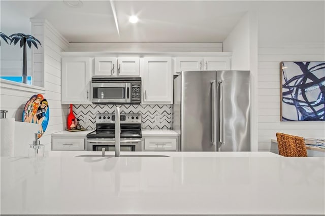 kitchen with white cabinets, appliances with stainless steel finishes, light countertops, wood walls, and backsplash