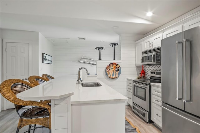 kitchen featuring a breakfast bar, stainless steel appliances, light countertops, white cabinetry, and a sink