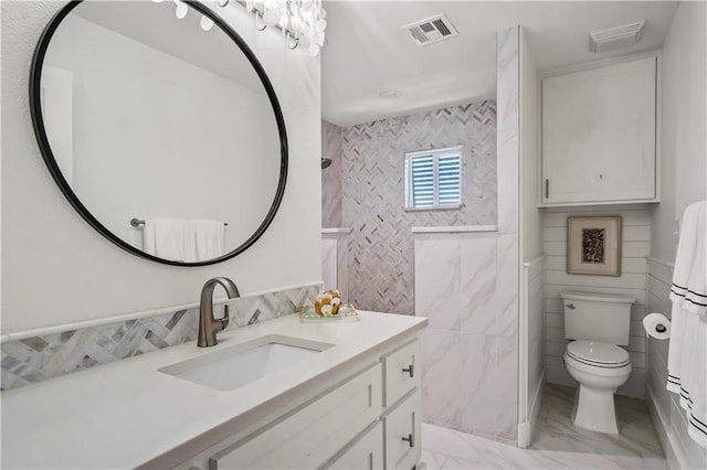 bathroom with visible vents, toilet, marble finish floor, vanity, and tile walls