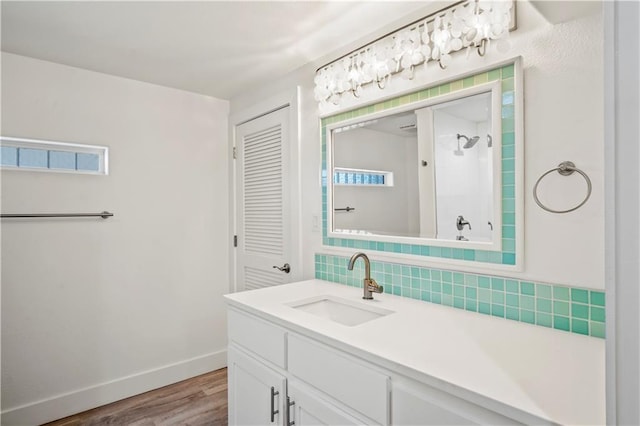 bathroom with wood finished floors, vanity, baseboards, a shower, and tasteful backsplash