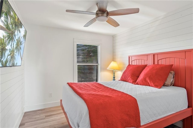 bedroom featuring ceiling fan, wood walls, light wood-style flooring, and baseboards