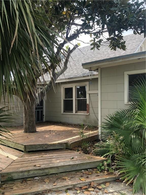 doorway to property with roof with shingles and a wooden deck