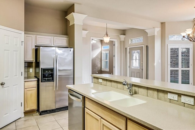 kitchen featuring light tile patterned floors, stainless steel appliances, a sink, hanging light fixtures, and decorative columns