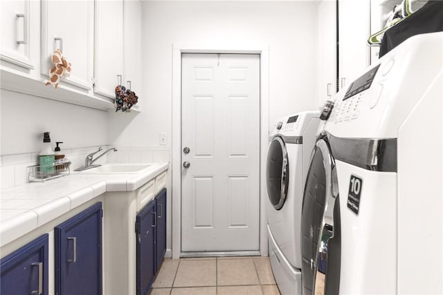 clothes washing area with washing machine and dryer, sink, light tile patterned flooring, and cabinets