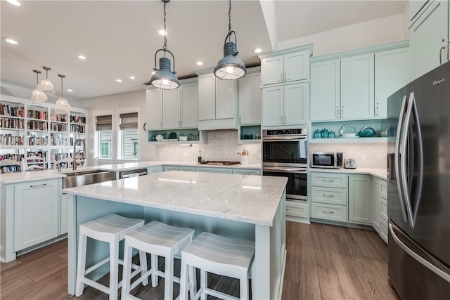 kitchen with appliances with stainless steel finishes, hanging light fixtures, sink, and dark hardwood / wood-style floors