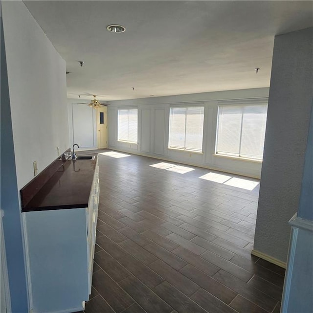 unfurnished living room with dark wood-style floors, a ceiling fan, and a sink