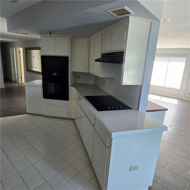 kitchen with light tile patterned floors, white cabinets, black electric cooktop, light countertops, and under cabinet range hood