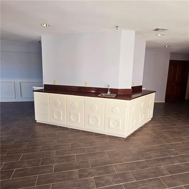 unfurnished room with visible vents, a sink, wood tiled floor, a decorative wall, and indoor wet bar