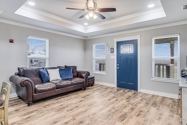 living area featuring a raised ceiling, light wood-style flooring, and baseboards