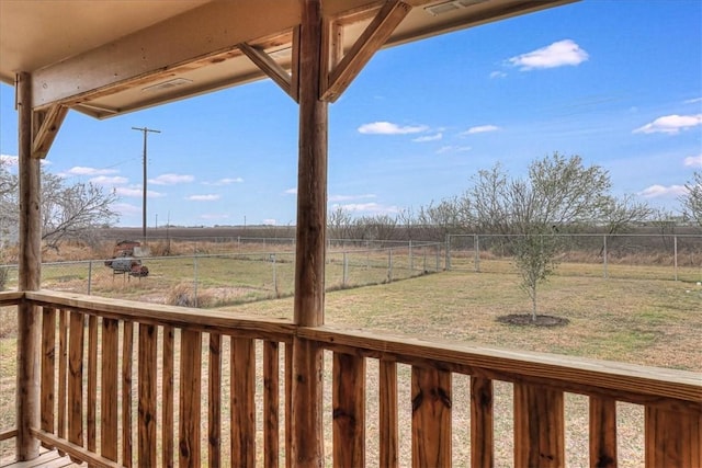 wooden terrace featuring a rural view, a lawn, and fence