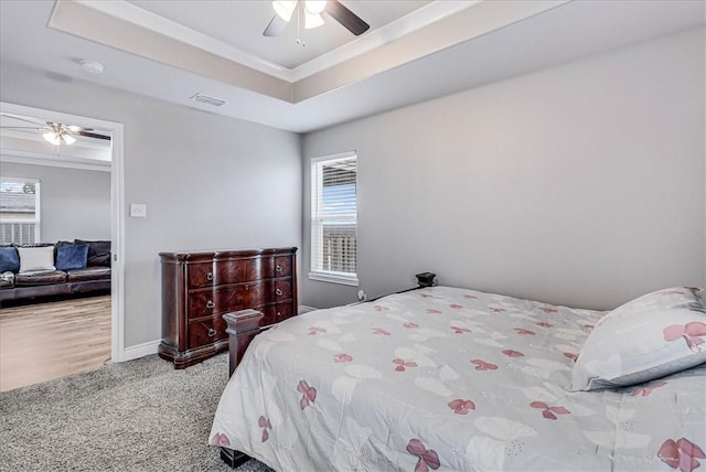 carpeted bedroom with a raised ceiling, visible vents, ornamental molding, ceiling fan, and baseboards