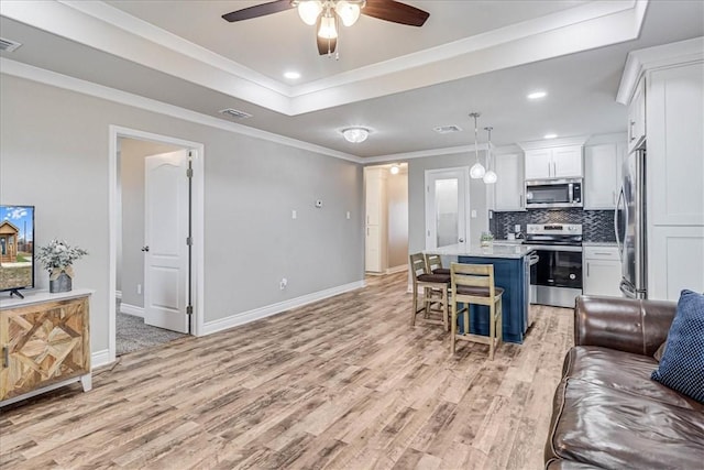 living area with light wood finished floors, visible vents, a tray ceiling, and crown molding