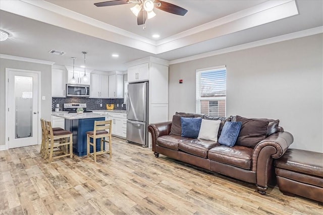 living room featuring a tray ceiling, crown molding, visible vents, light wood-style flooring, and a ceiling fan