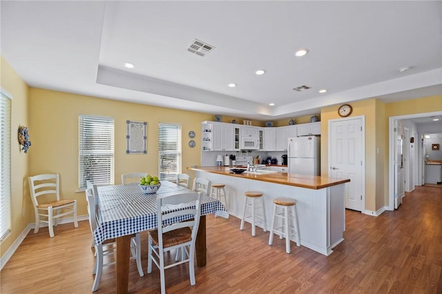 kitchen with white appliances, a peninsula, glass insert cabinets, a kitchen bar, and light wood-type flooring