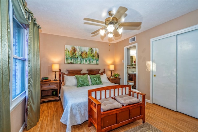 bedroom featuring ensuite bath, ceiling fan, light wood-type flooring, a textured ceiling, and a closet